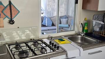 A kitchen with a gas stove, two sinks, a window with curtains, and a view of a living area.