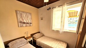 A small room with two beds, a nightstand, a painting on the wall, and a window with curtains. - Villa Bonaca (Marina)
