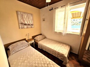 A small room with two beds, a nightstand, a painting on the wall, and a window with curtains. - Villa Bonaca (Marina)