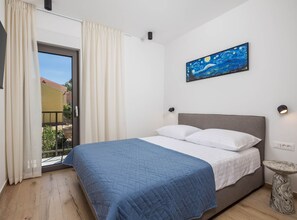 A bedroom with a bed, a painting, a window with curtains, and a small table. - Apartments Villa Mara With Pool (Omisalj)
