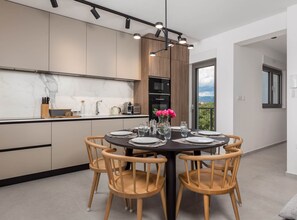 Una cocina moderna con comedor, que incluye una mesa redonda con sillas, vistas al exterior y electrodomésticos integrados.
