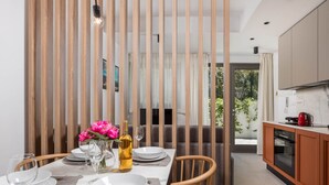 A modern kitchen with a dining area, wooden vertical blinds, and a view of greenery outside. - Apartments Villa Mara With Pool (Omisalj)