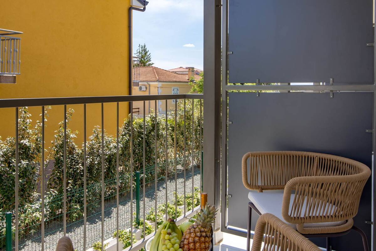 A balcony with a yellow wall, wicker chairs, and a view of a red-roofed building.