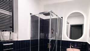 Un baño moderno con ducha envuelta en vidrio, inodoro blanco, piso de baldosas blanco y negro, y un espejo redondo.