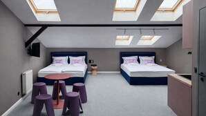 Un dormitorio moderno con tragaluces, dos camas, una mesita redonda y taburetes morados.