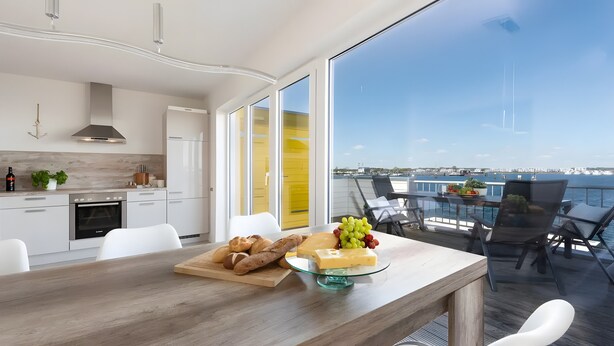 A modern kitchen with white cabinets, a wooden dining table with a glass top, and a view of the marina through large windows. - Nothing Beats the Sea – 2-Bedroom Apartment for 5 with Harbor View in Kappeln (Kappeln)
