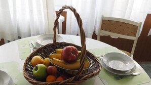 Uma mesa de jantar com uma cesta de frutas, uma cadeira e um prato.