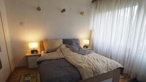 Um quarto com uma cama, duas mesas de cabeceira com luminárias, uma janela com cortinas e um tapete estampado.