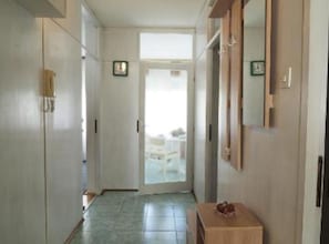 En hall med en dörr som leder ut till en balkong, ett litet bord med en korg och en klocka på väggen.