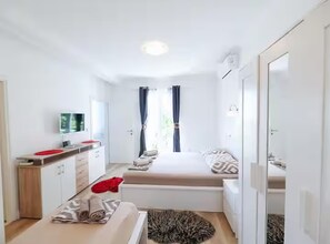 A compact hotel room with a bed, a small desk, a mirror, and a window with curtains. - Deluxe Apartment Marghareta (Dubrovnik)