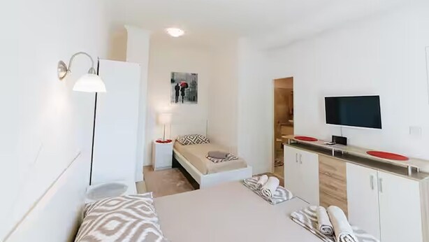 A modern, well-lit room with a bed, bedside table, lamp, and a TV mounted on the wall. - Deluxe Apartment Marghareta (Dubrovnik)