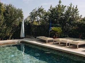 A swimming pool with lounge chairs and umbrellas, surrounded by greenery. - Deluxe Apartment Marghareta (Dubrovnik)