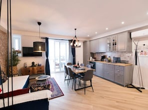 Una cocina moderna con armarios grises, un comedor con mesa redonda y una sala de estar con sofá y televisor.