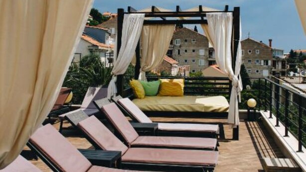 Un balcón con cama con dosel, sillones de descanso y vistas a edificios.