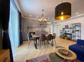 A modern living room with a dining area, a blue sofa, a coffee table, and a kitchen in the background. - Residence Apartment Marghareta No. 2 (Dubrovnik)