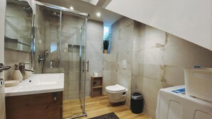 Un baño moderno con cabina de ducha de vidrio, tocador de madera, inodoro y cubo de basura.