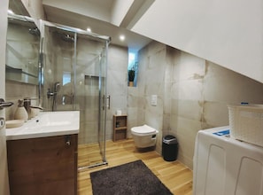 A modern bathroom with a glass shower enclosure, a wooden vanity, a toilet, and a trash bin. - Residence Apartment Marghareta No. 2 (Dubrovnik)
