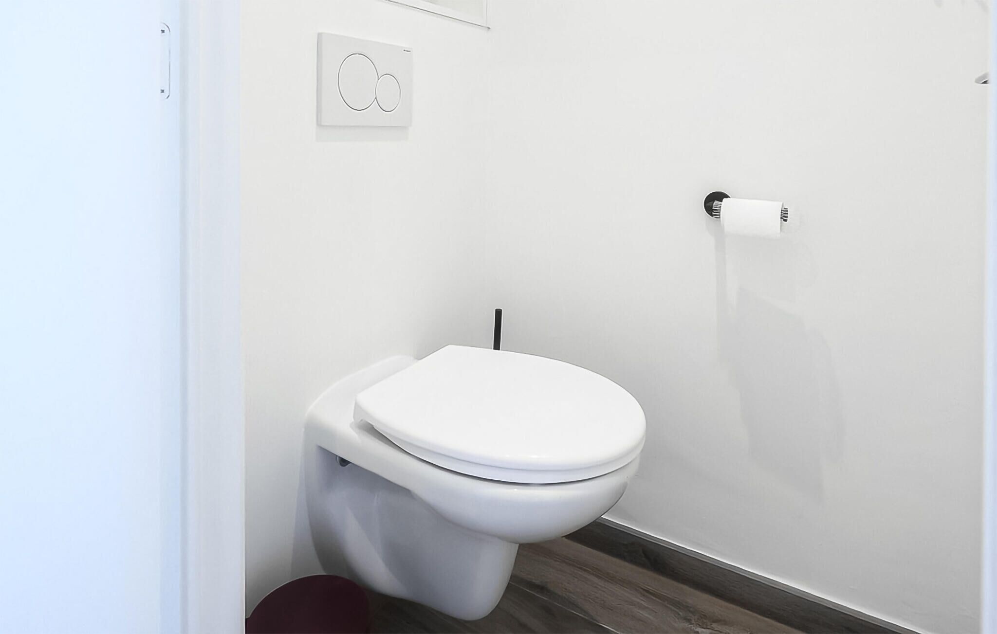 Sanitário moderno com assento e tampa brancos, barra de descarga na parede e uma pequena lixeira.