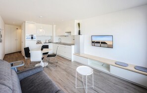 Eine moderne Küche mit weißen Schränken, ein Essbereich mit Tisch und Stühlen, eine Couch und ein kleiner weißer Hocker.