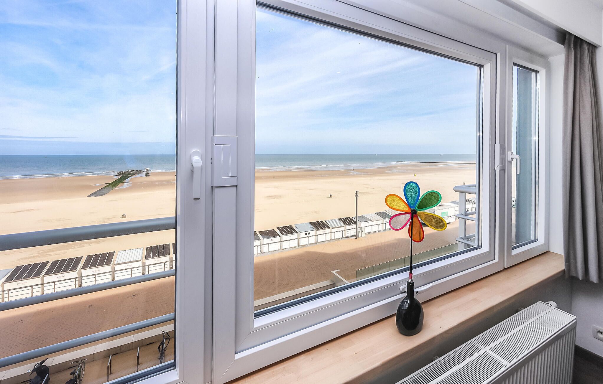 Quarto com uma grande janela com vista para a praia, um enfeite de pinwheel e um radiador.