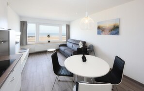 Eine moderne Küche mit Essbereich, einem grauen Sofa und einem Strandbild.
