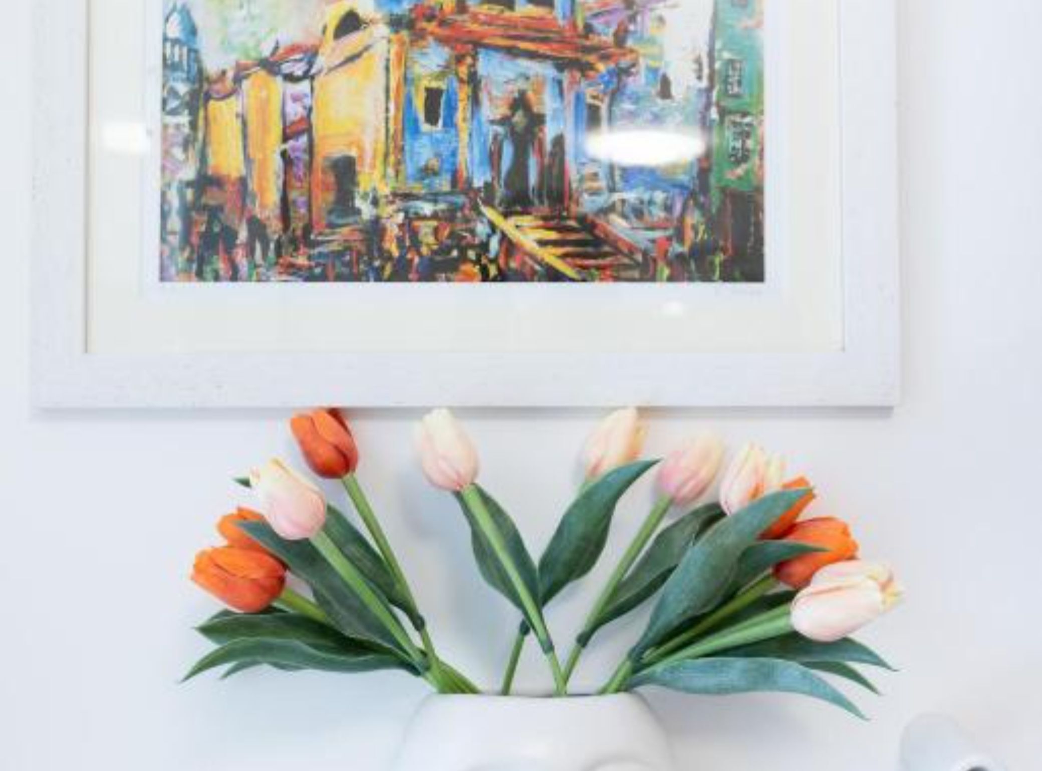 Ein gerahmtes Gemälde, das eine farbenfrohe Straßenszene zeigt, darunter ein Strauß Tulpen.