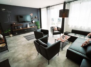 Una sala de estar moderna con un sofá, sillones, una mesa de centro, un televisor y una estantería.