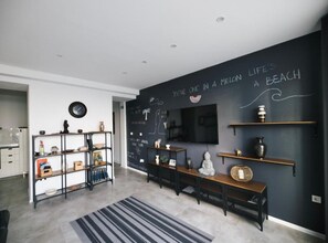 Una sala moderna con una pared de pizarra, estantes de madera y un televisor.