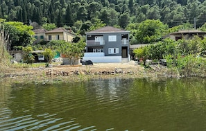 Een twee verdiepingen tellend huis met een balkon, gelegen aan het water, omringd door groen.