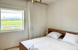 Quarto com cama, janela com cortinas e vista para um campo e montanhas.