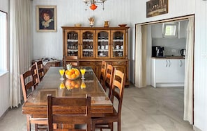 Een eetkamer met een houten tafel, stoelen, een schaal fruit en een kast met glazen deuren.