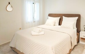A neatly made bed with a white duvet and two pillows, a small bedside table with a lamp, and a window with sheer curtains. - 1 bedroom amazing home in Pupnat (Pupnat)