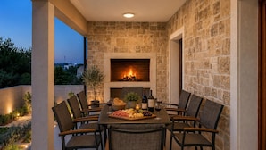 Un área de comedor al aire libre con una chimenea de piedra, una mesa dispuesta con comida y bebidas, y sillas.