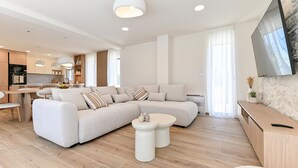 Ein modernes Wohnzimmer mit Ecksofa, Essbereich, Küche und einem an der Wand befestigten Fernseher.