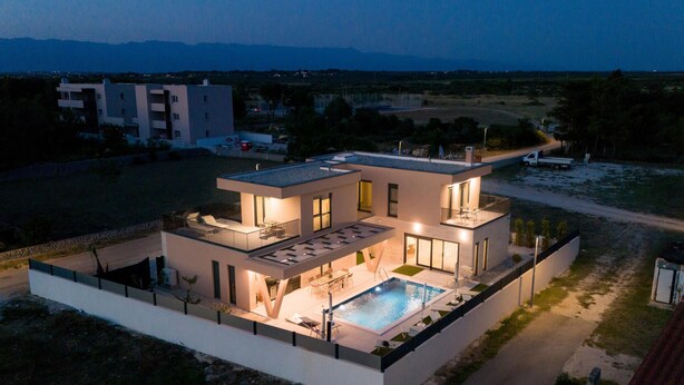Ein modernes, zweistöckiges Haus mit Swimmingpool, großen Fenstern und einer Flachdach.