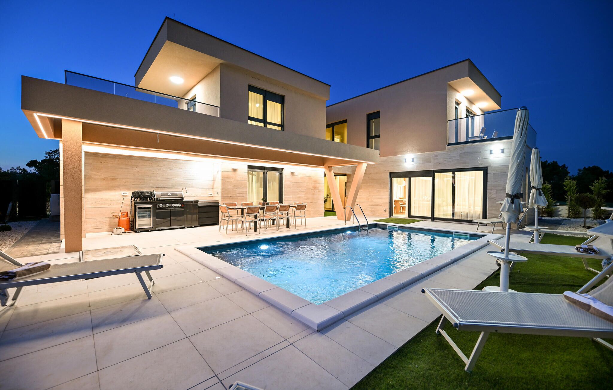 A modern two-story house with a swimming pool, outdoor seating, and a barbecue area.