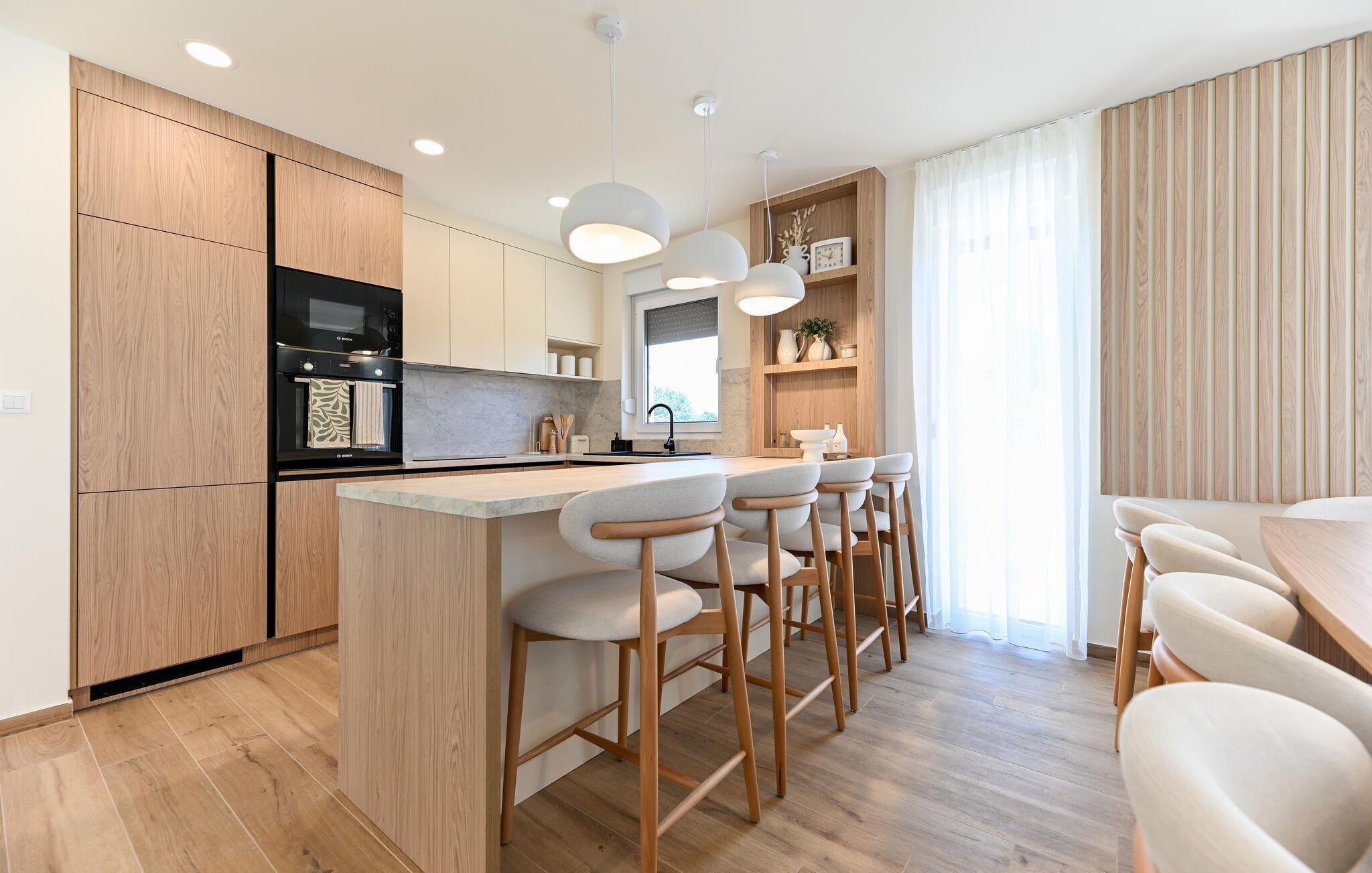 A modern kitchen with wooden cabinets, a built-in oven, and a bar area with bar stools.
