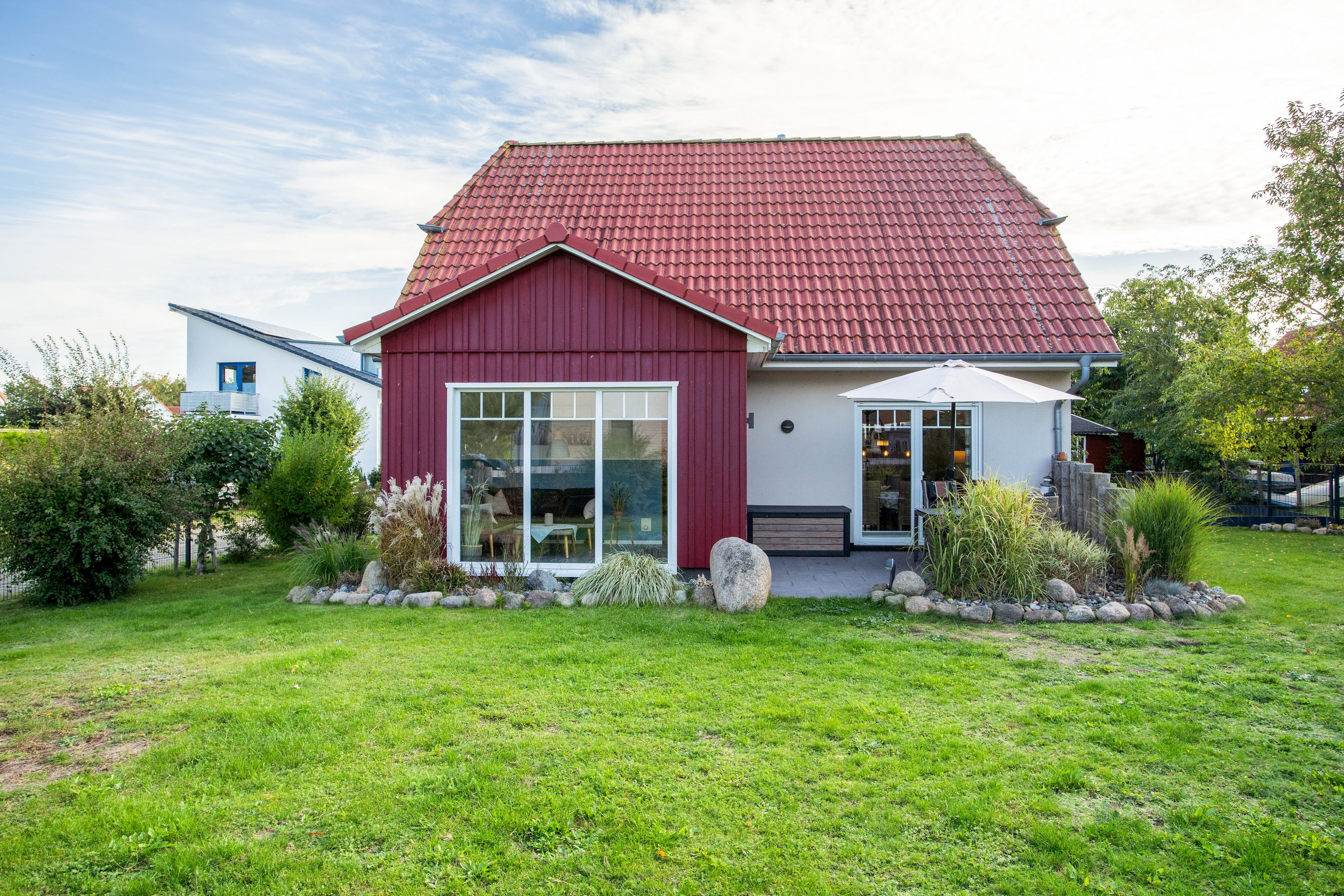 A modern house with a red roof, large windows, and a well-maintained garden.