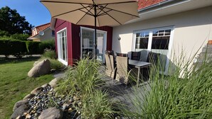 A patio with outdoor furniture, a large umbrella, and a stone pathway leading to a house with a red exterior and white trim. - Holiday Home for 6 Guests, 123 m², Private Terrace, Free Wi-Fi (Fuhlendorf)