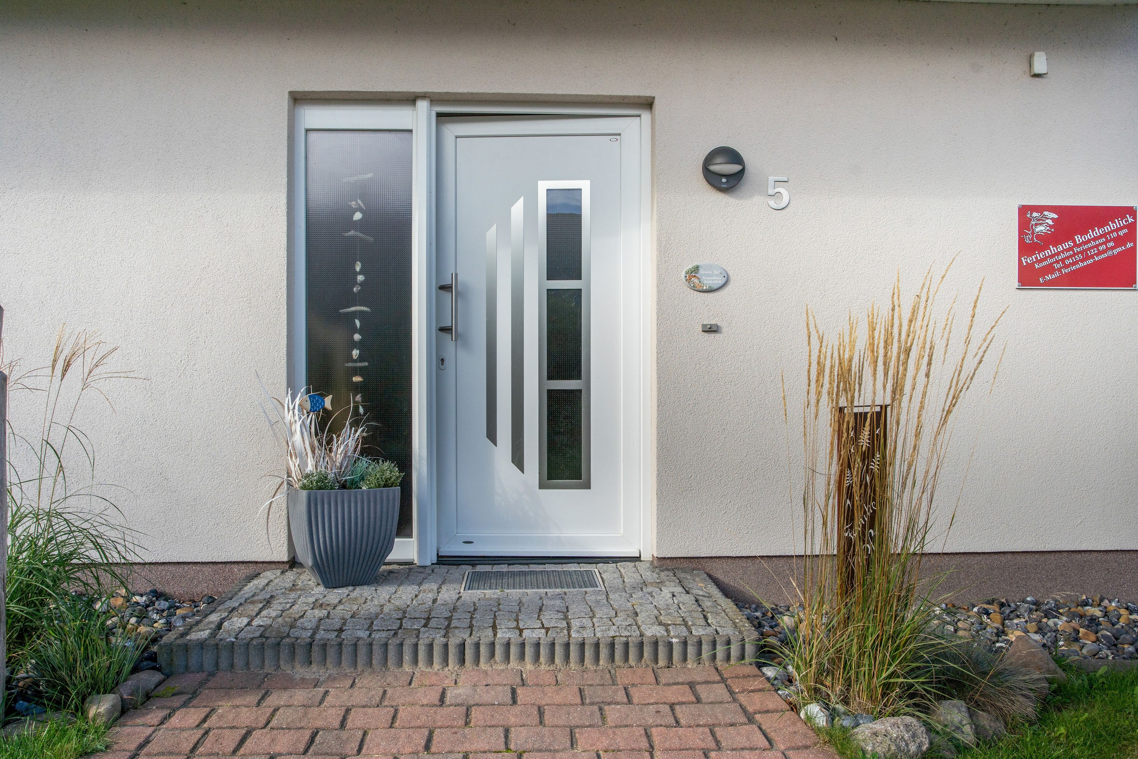 A building entrance with a double door, a potted plant, and a signboard.