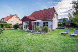 A residential house with a red roof, a glass door entrance, and a well-maintained lawn with two lounge chairs.