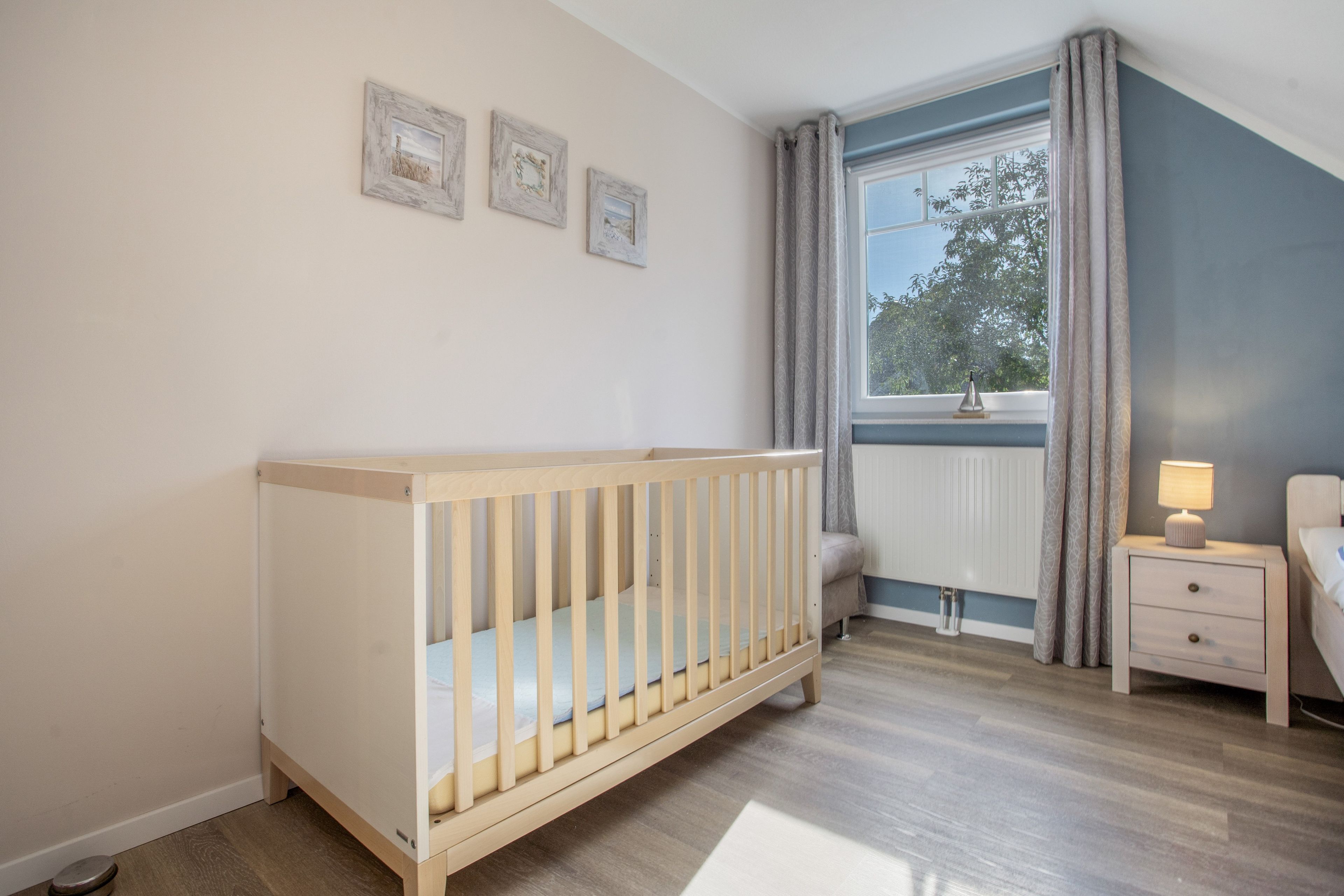 A baby room with a crib, a bedside table with a lamp, and a window with curtains.