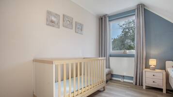 A baby room with a crib, a bedside table with a lamp, and a window with curtains.