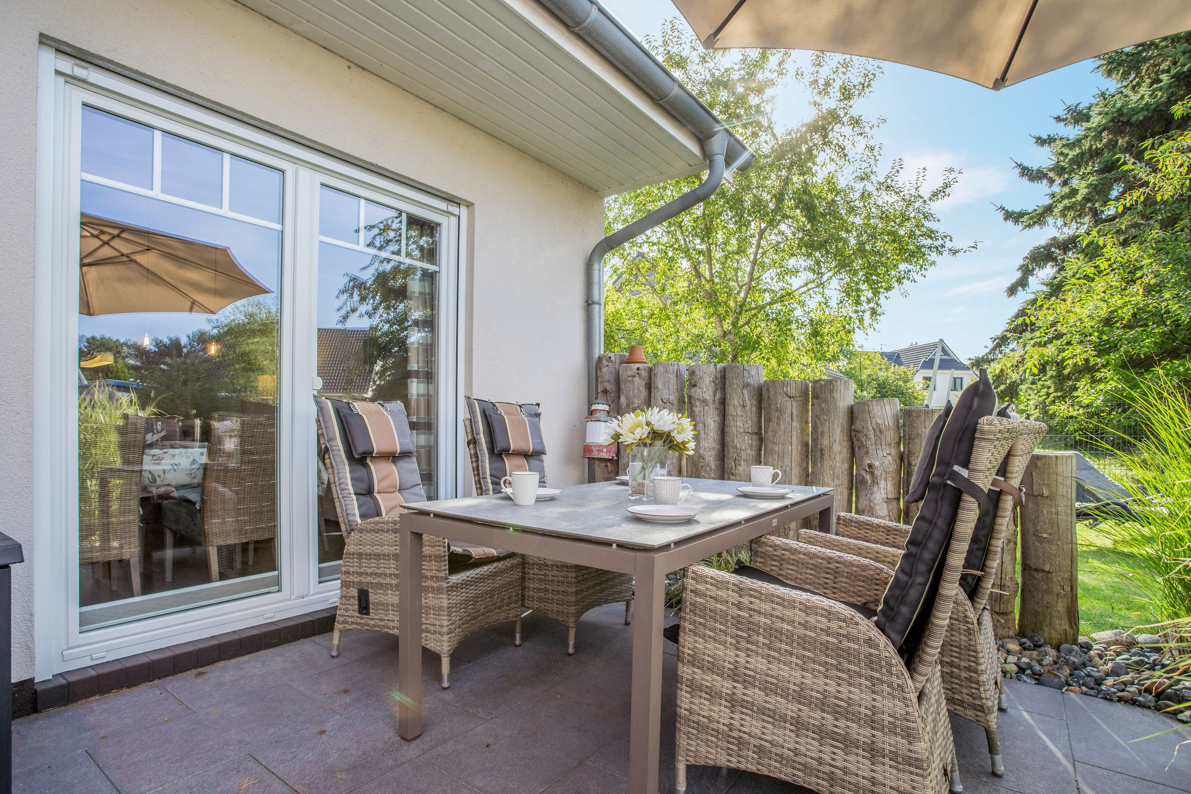 An outdoor patio with a table and chairs, a glass door, and a wooden fence.