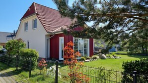 A two-story house with a red roof, a white facade, and a fenced yard with a small garden and a statue. - Holiday Home for 6 Guests, 123 m², Private Terrace, Free Wi-Fi (Fuhlendorf)