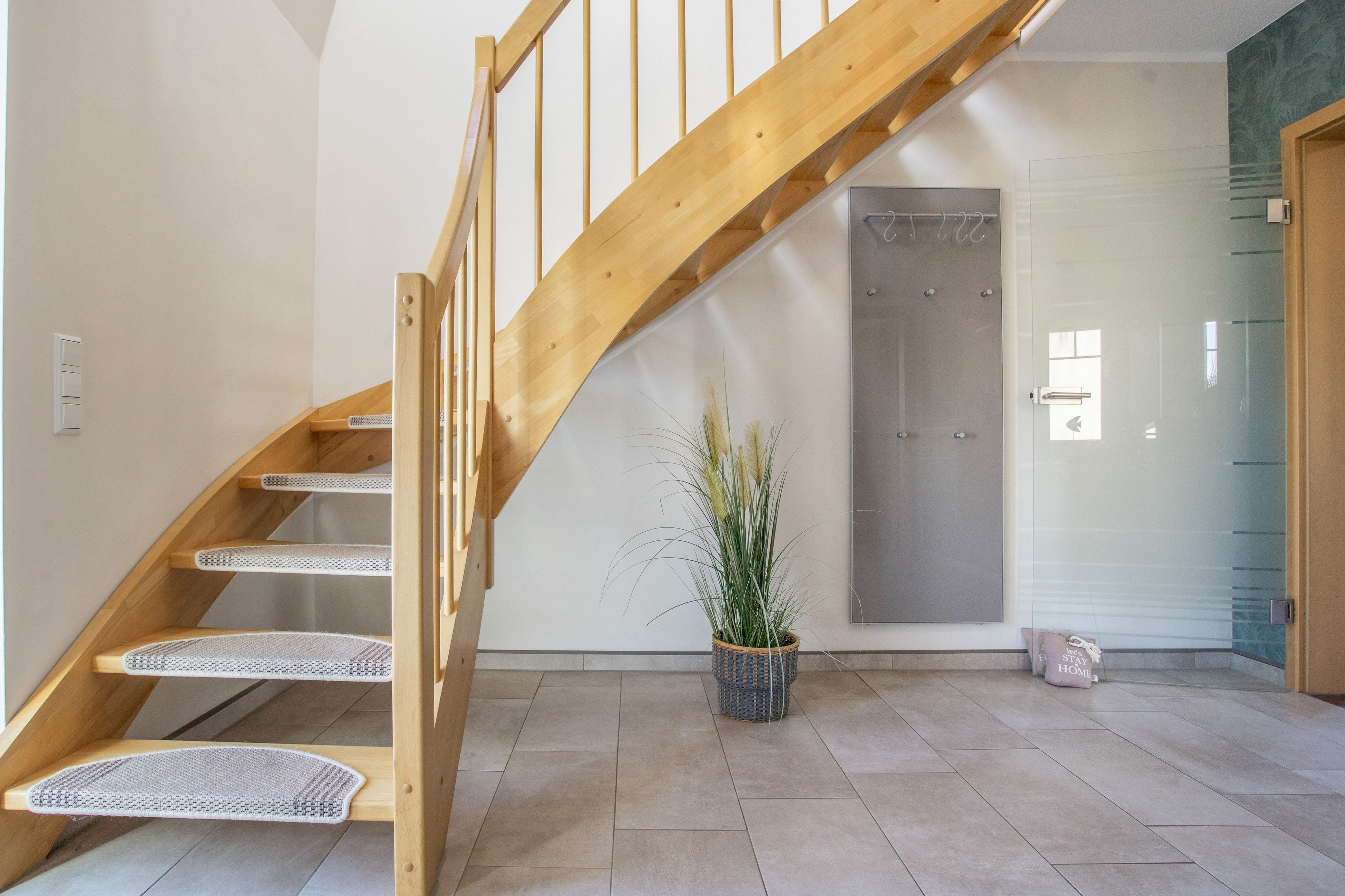 A wooden staircase with a handrail, leading to a room with a tiled floor and a potted plant.