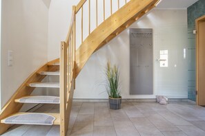 Una escalera de madera con barandilla que lleva a una habitación con piso de baldosas y una planta en maceta.