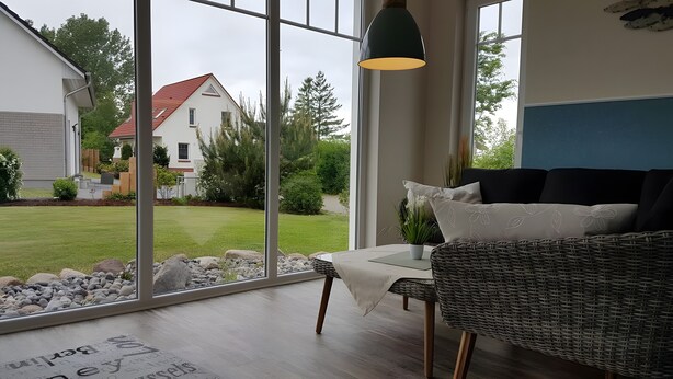 A room with a large window, a wicker sofa, a table, and a hanging light fixture. - Holiday Home for 6 Guests, 123 m², Private Terrace, Free Wi-Fi (Fuhlendorf)