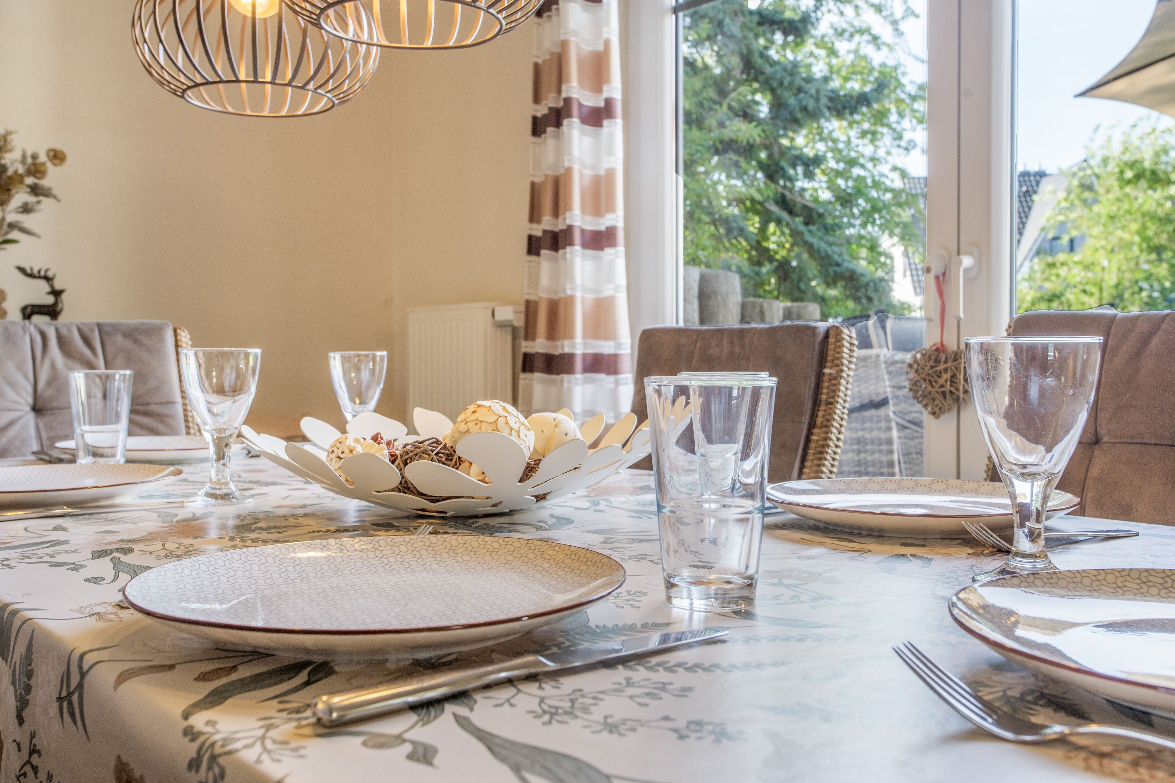 A dining table set with plates, glasses, and cutlery, with a decorative bowl and a candle holder on the table.