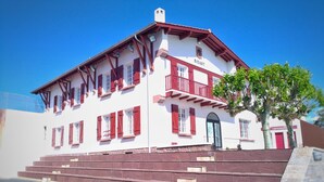 Ein zweistöckiges Gebäude mit roter und weißer Fassade, einem Balkon und einer Treppe, die zum Eingang führt.